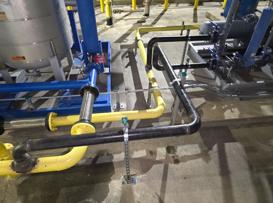 Industrial pipes and valves in a factory, with yellow and black insulated piping on a concrete floor