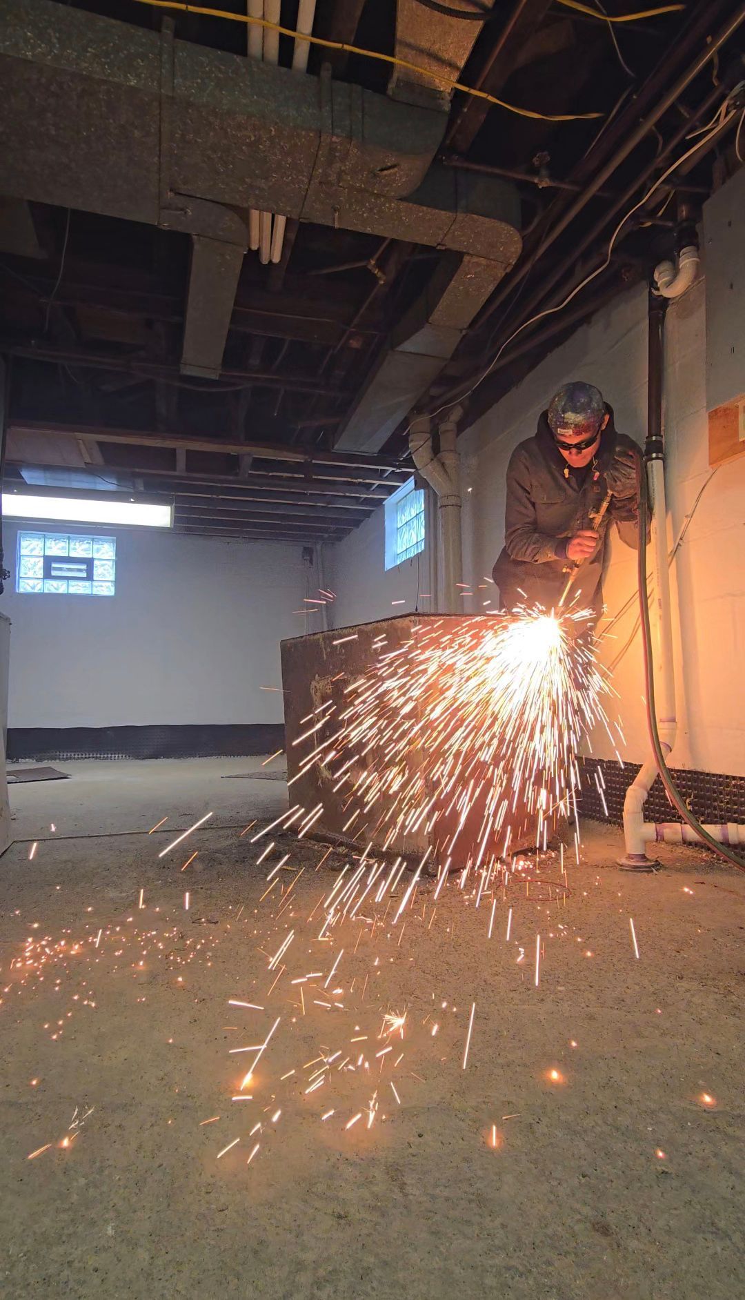 A worker welding metal, sending bright sparks across a dim industrial room