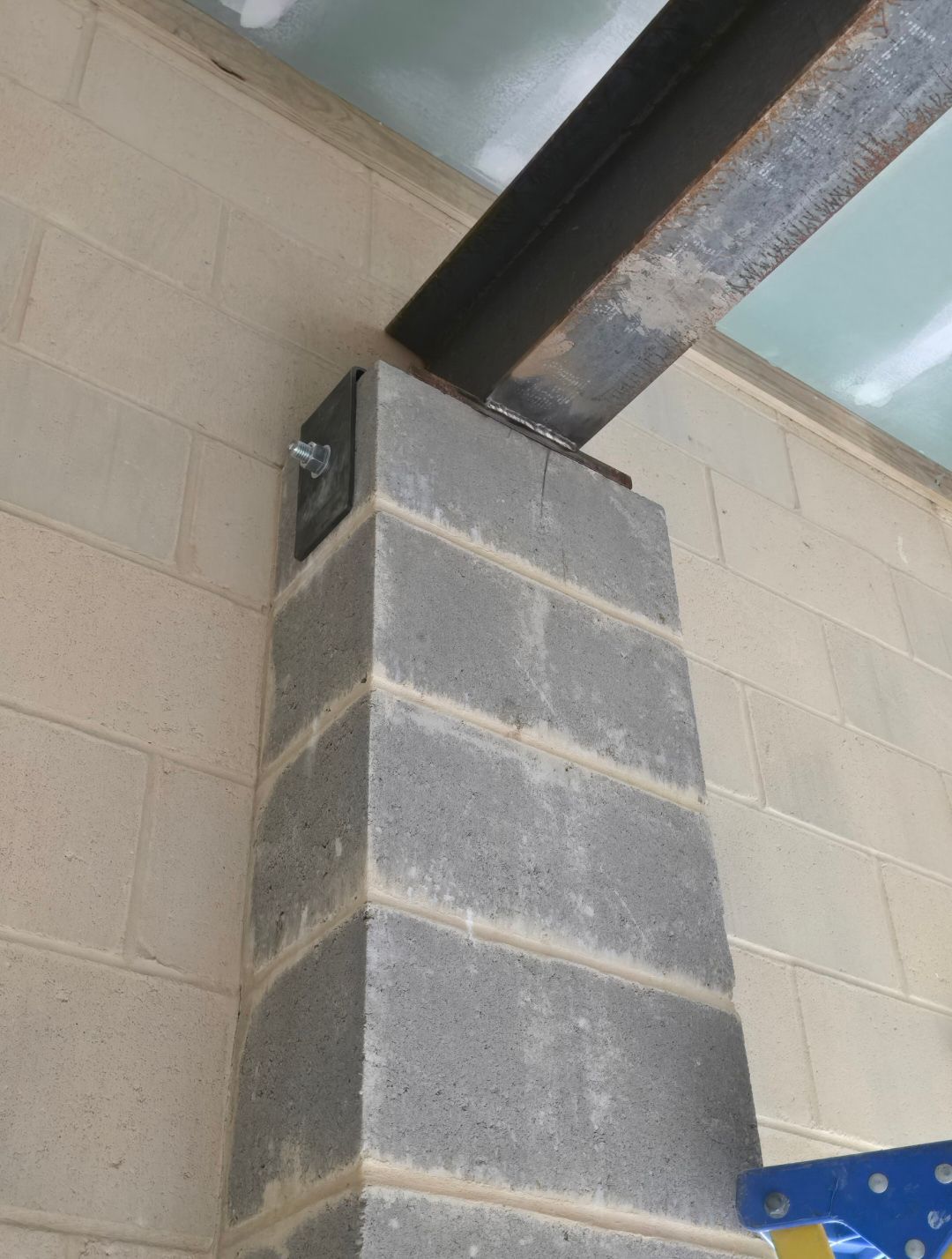 Concrete pillar supporting a steel beam in an industrial interior, with a blue metal bracket beside it