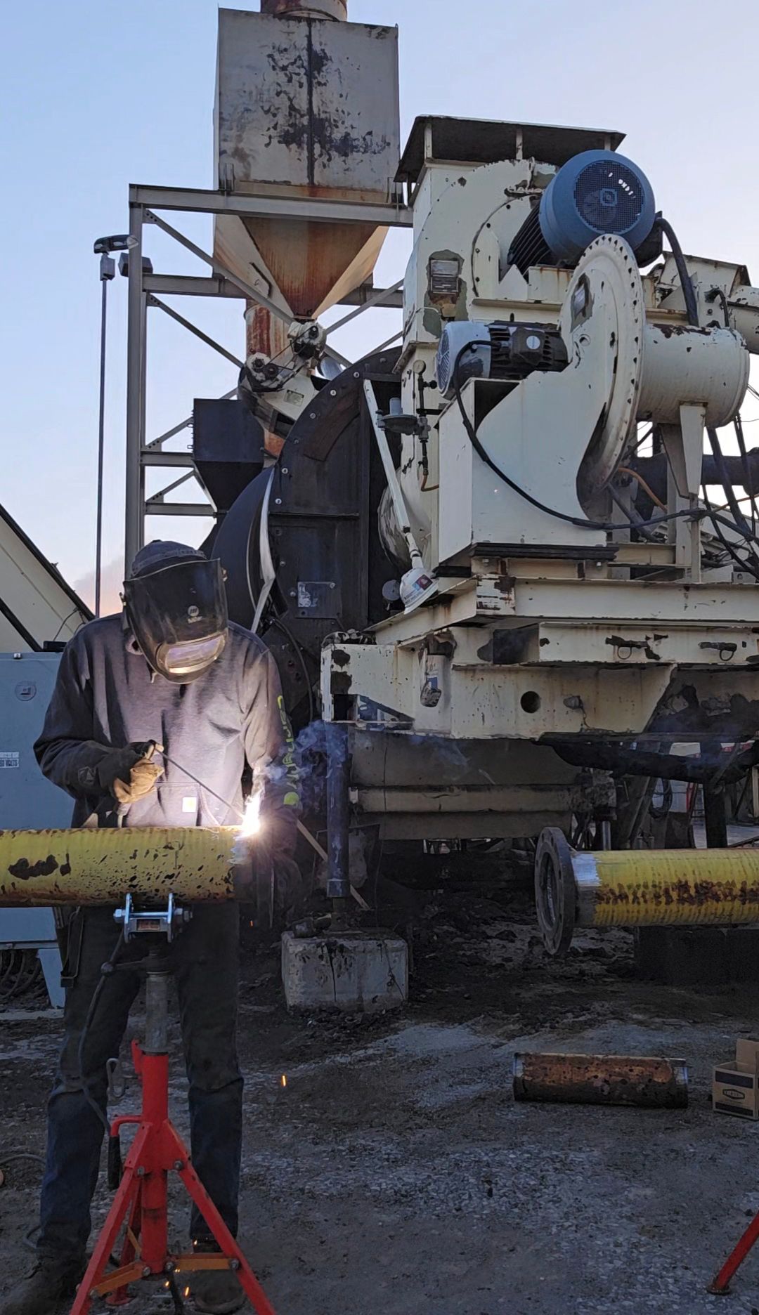 Worker welding beside a concrete mixer truck at a construction site, sparks flying from the torch.