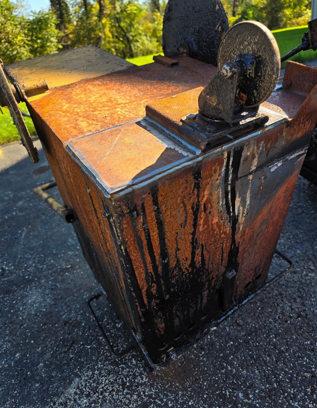 Rusty orange metal dumpster with black stains and circular lids outdoors on pavement.