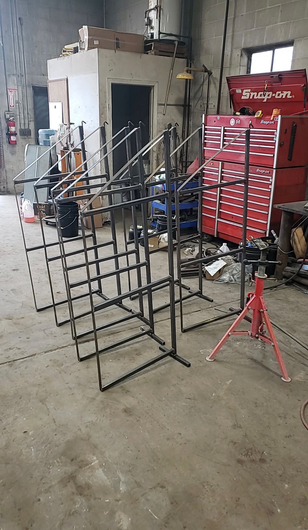 Workshop with metal racks and equipment, a red tool chest, and a white cabinet on a concrete floor.