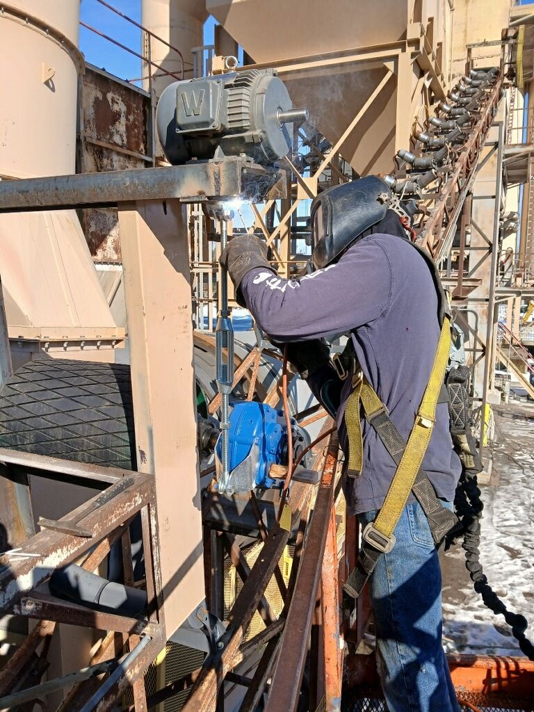 Worker in blue jacket and hard hat inspecting industrial equipment on a metal platform.