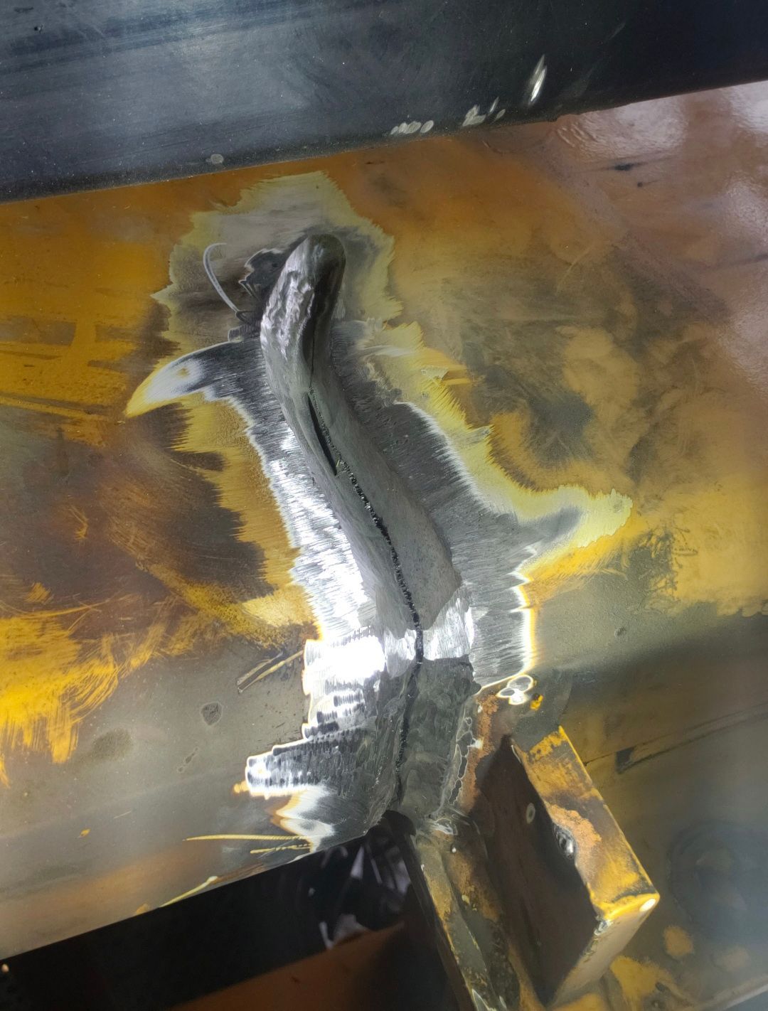 Close-up of a welded metal seam with silver bead and yellow-brown heat discoloration.