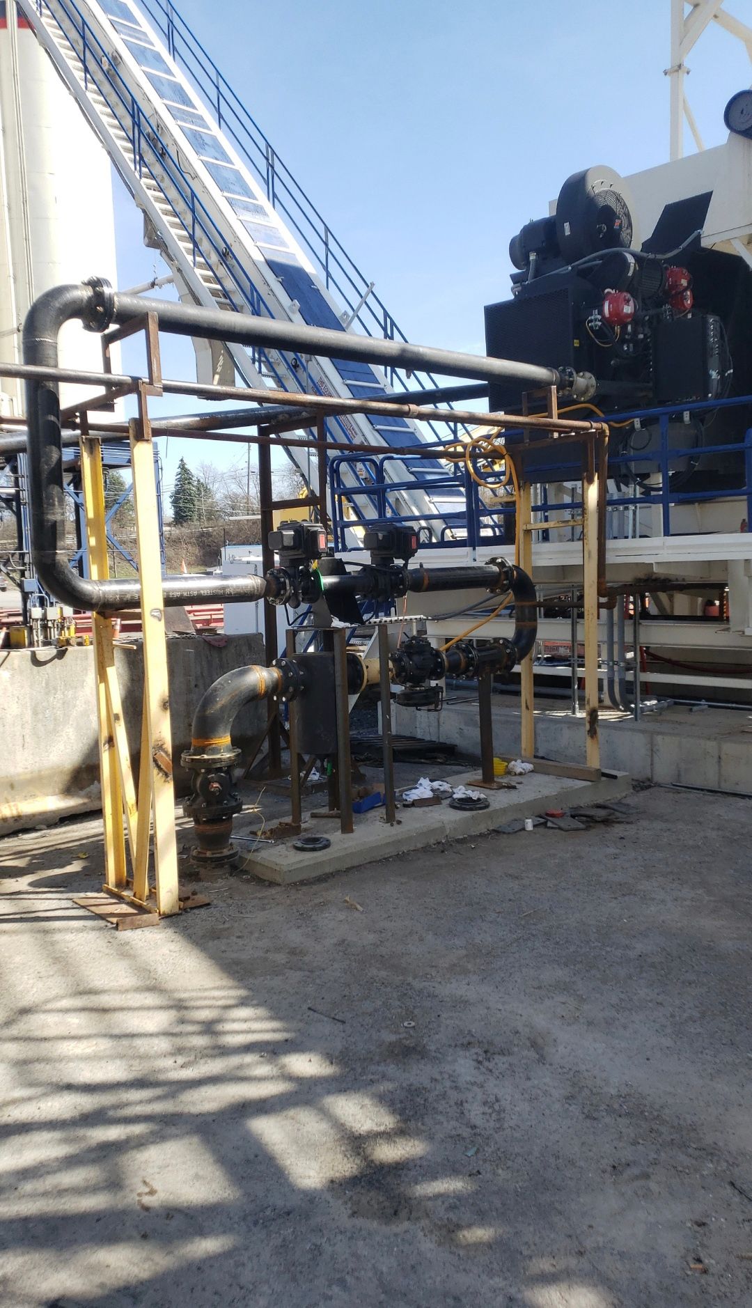 Industrial machinery with blue conveyor and black equipment on a gravel site under a clear sky