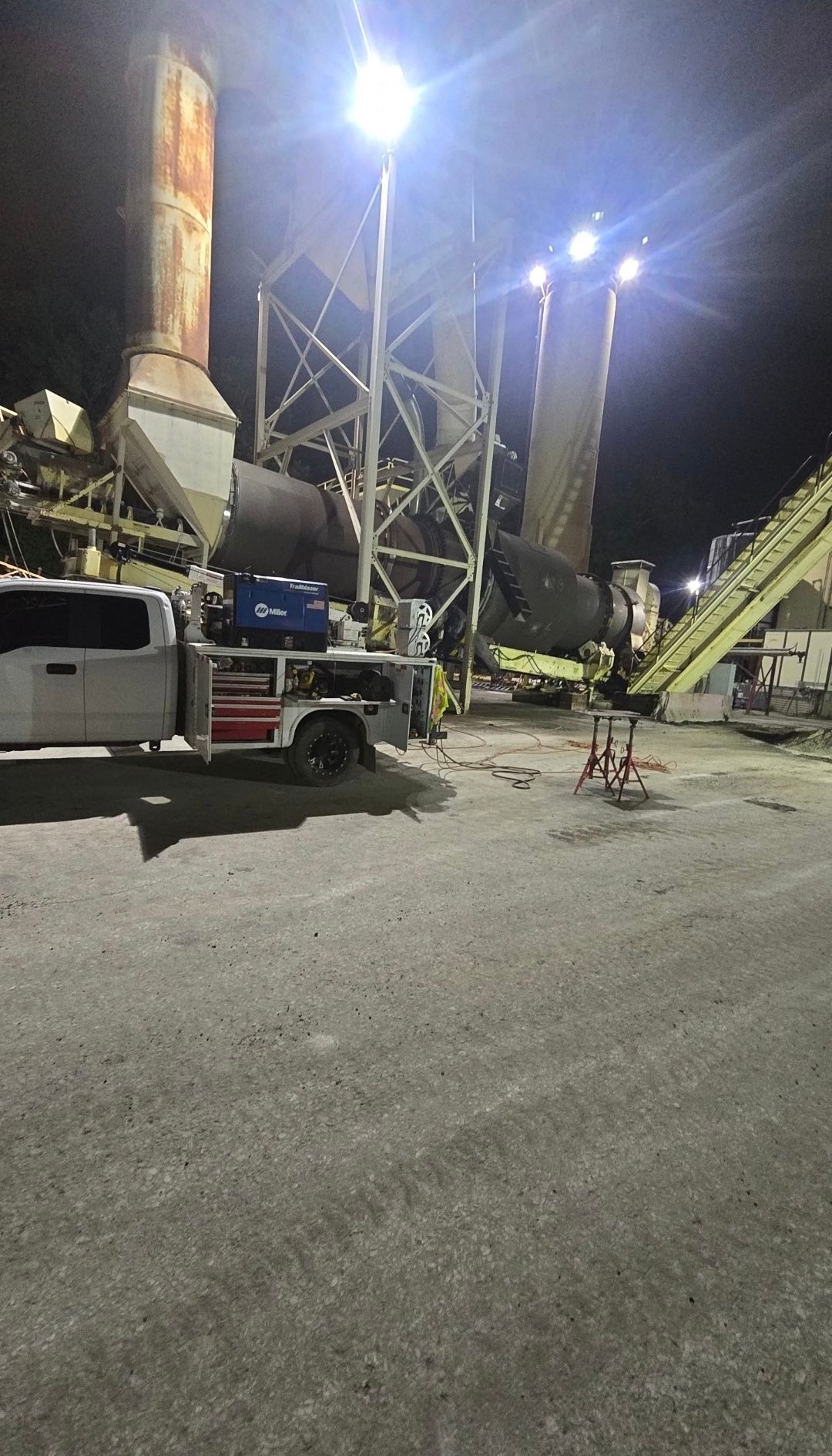 Nighttime construction site with a truck, tall industrial equipment, and bright floodlights illuminating the area