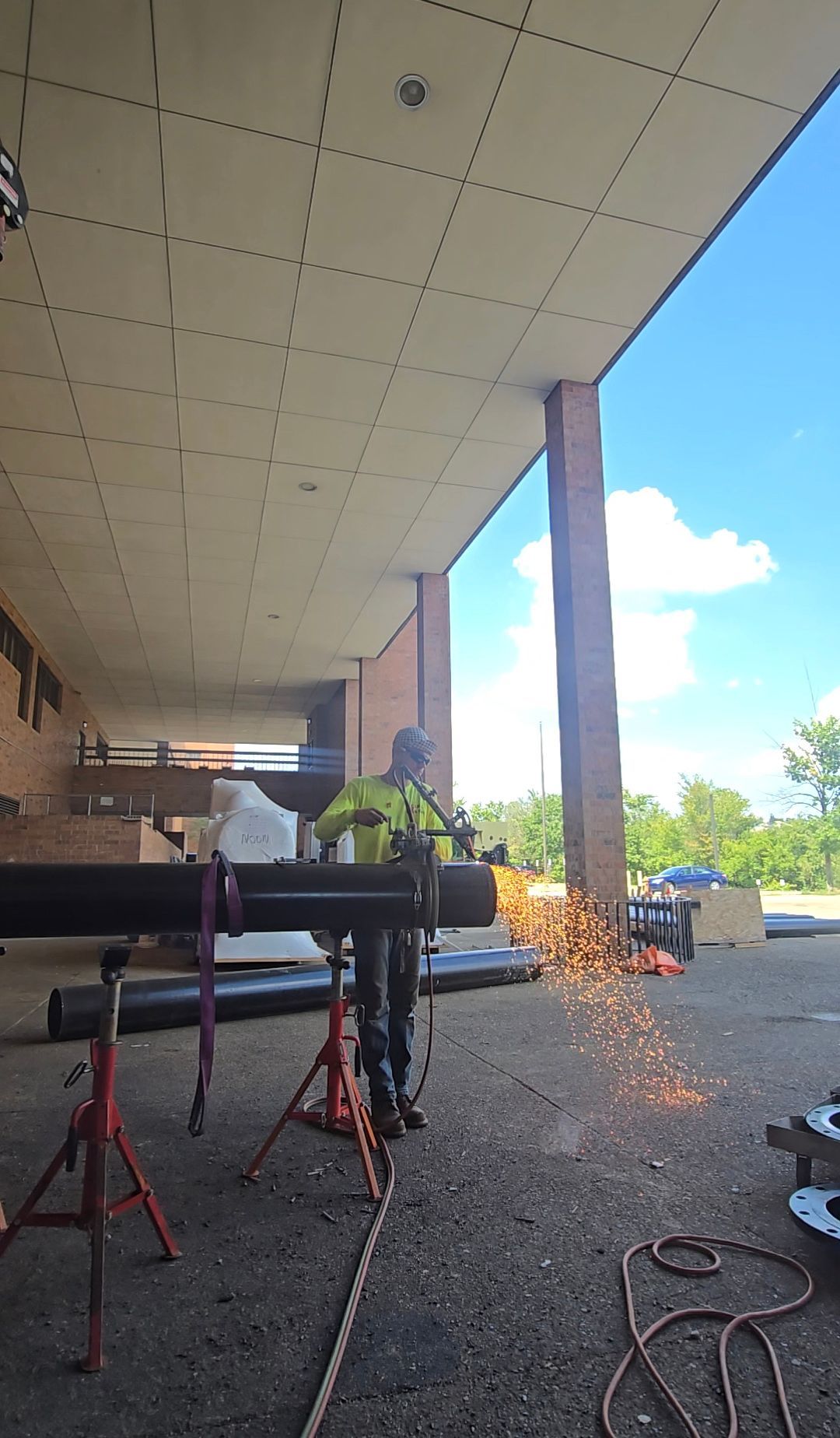 Outdoor covered walkway with construction equipment and sparks flying near a column, blue sky visible beyond.