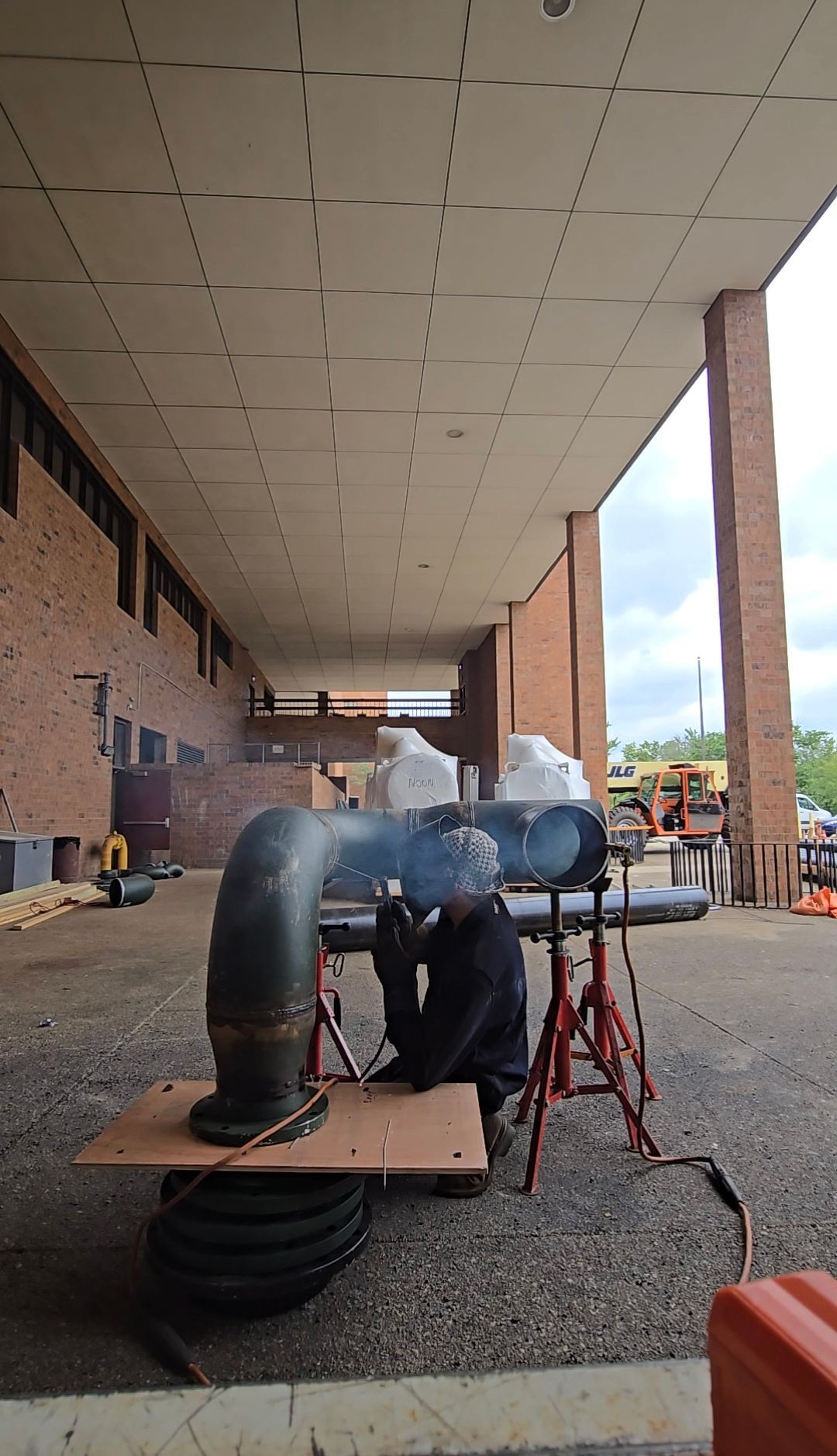 Outdoor walkway with large black pipes and maintenance equipment under a covered brick building entrance