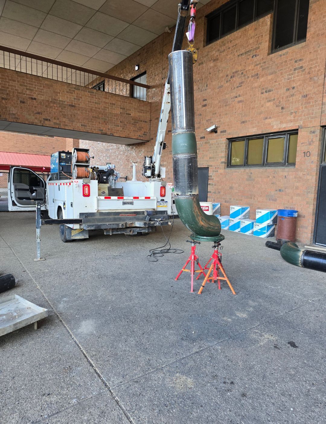 Industrial duct section on red stands beside a work truck in a brick building courtyard.