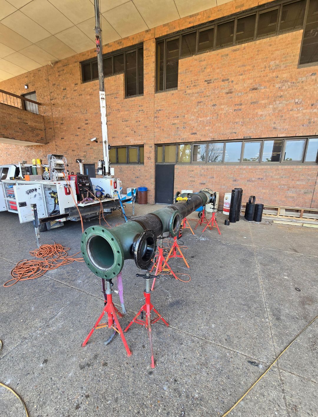 Large metal duct sections on red stands in a workshop with equipment against a brick wall