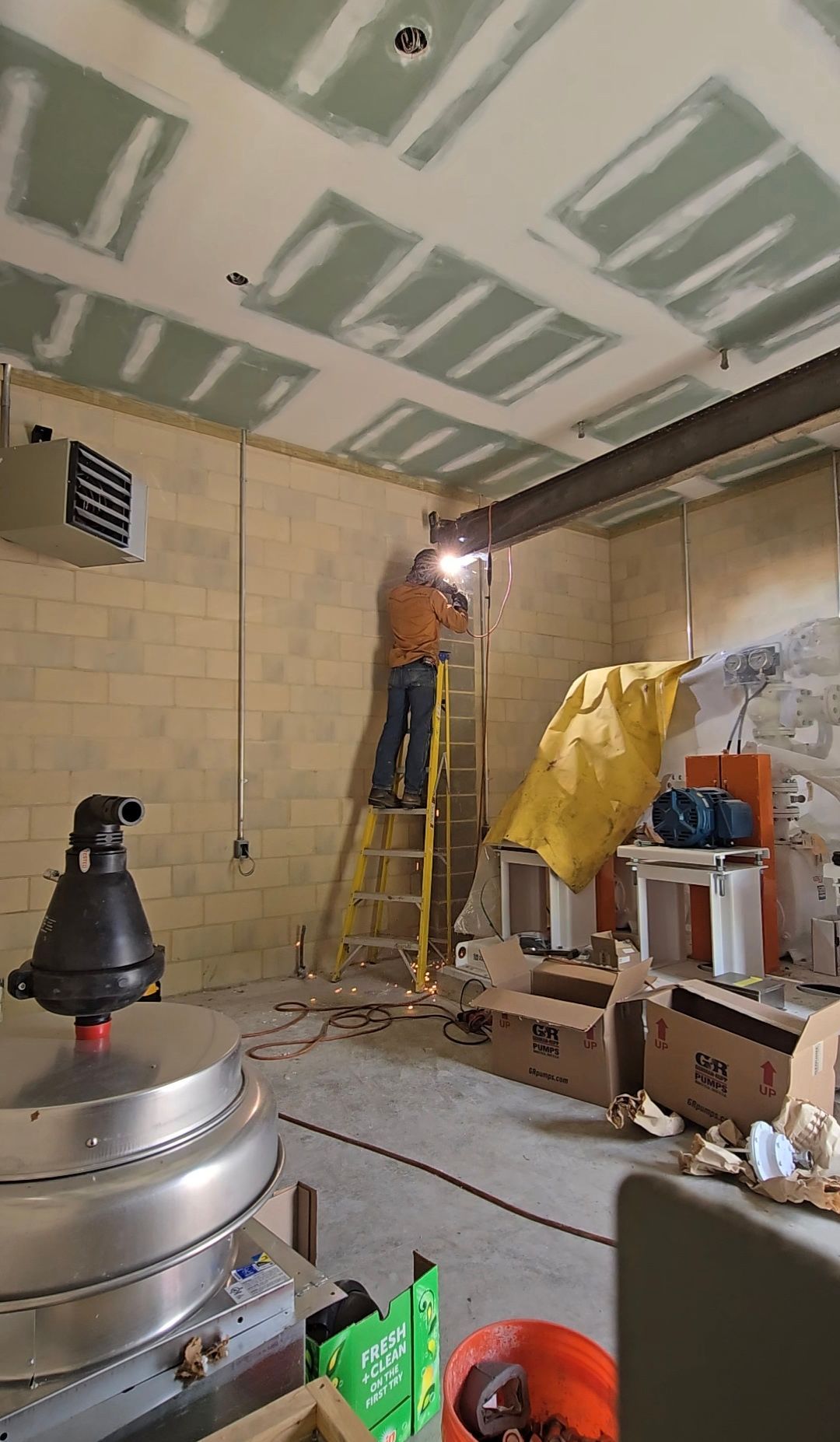 Person on ladder working on ceiling in a partially finished room with tools and materials scattered around