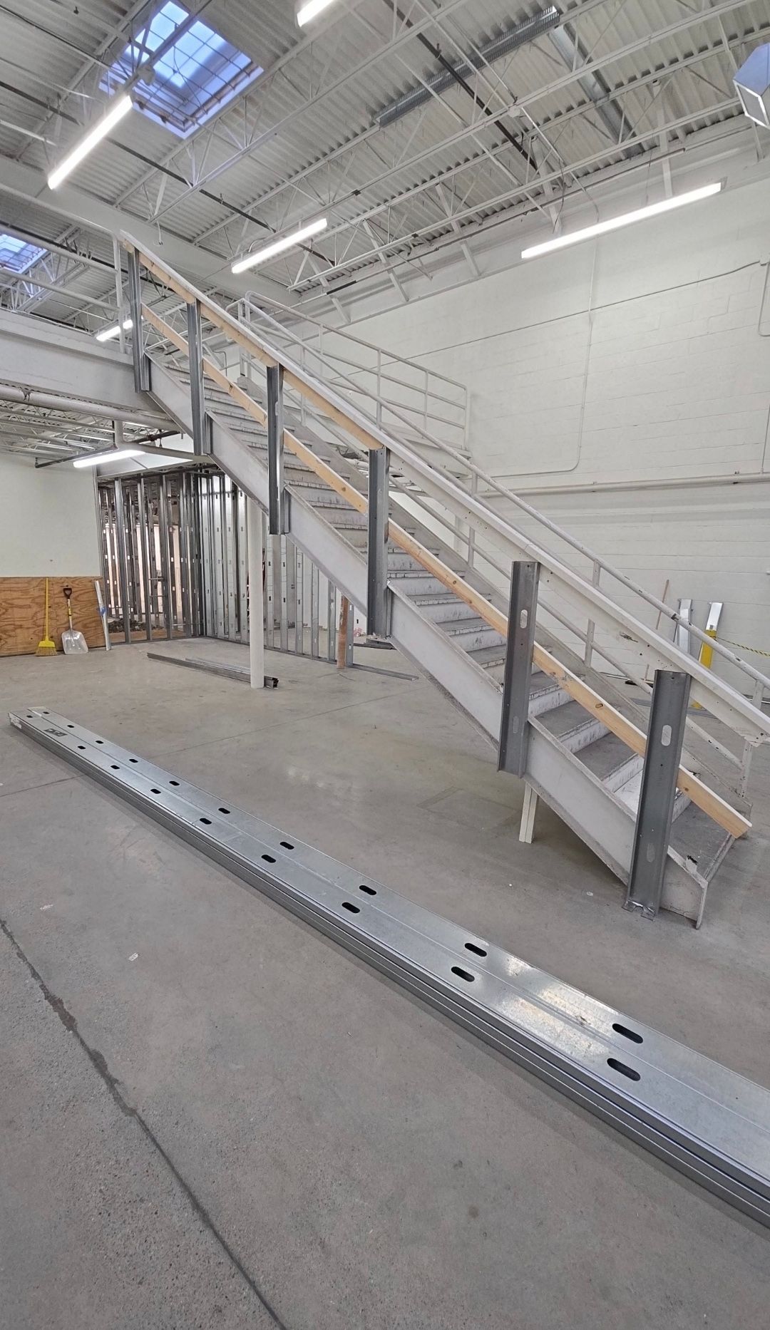 Indoor warehouse with a metal stairway, white walls, and a concrete floor under bright overhead lights.