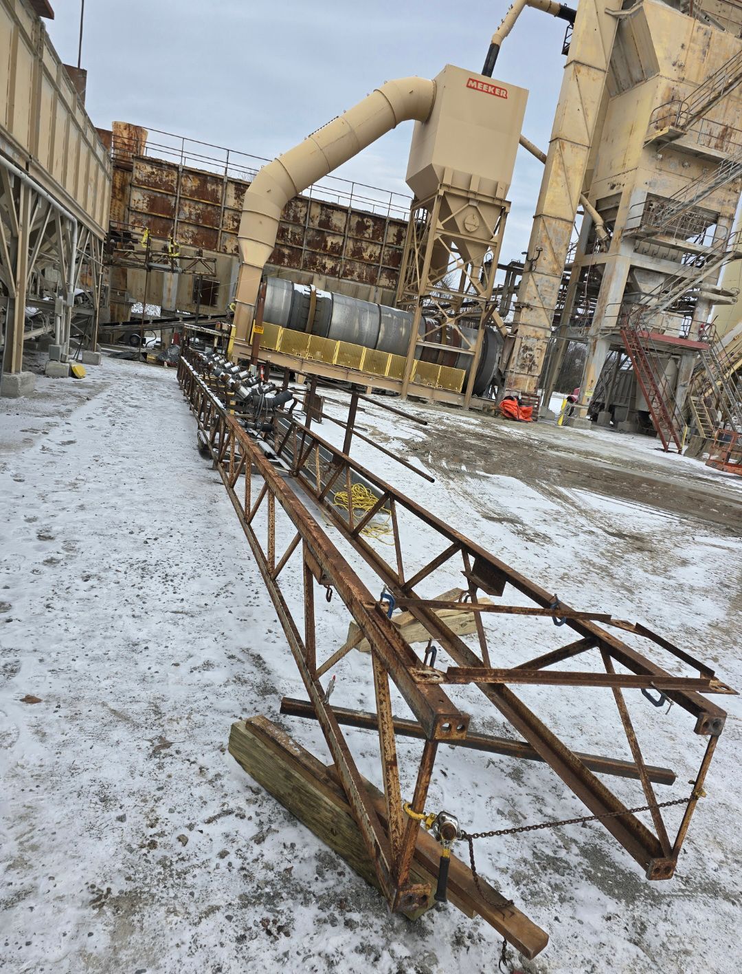 Snow-covered industrial site with damaged metal framework in the foreground and large machinery in the background