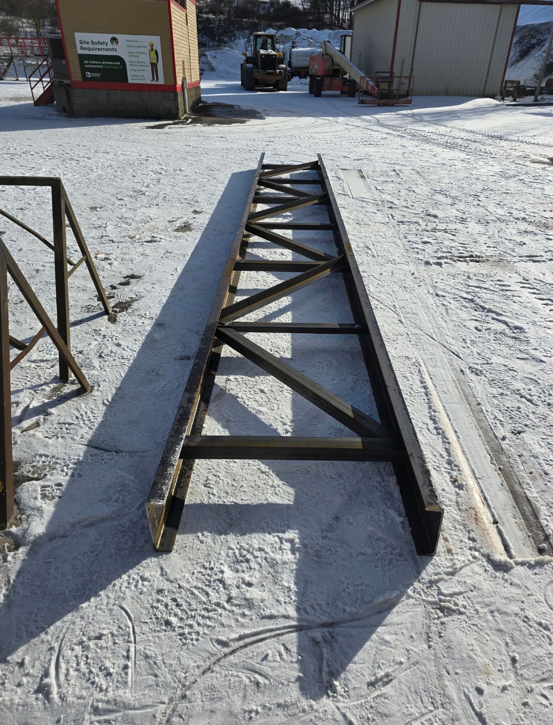 Black metal truss beams lying on a snowy ground