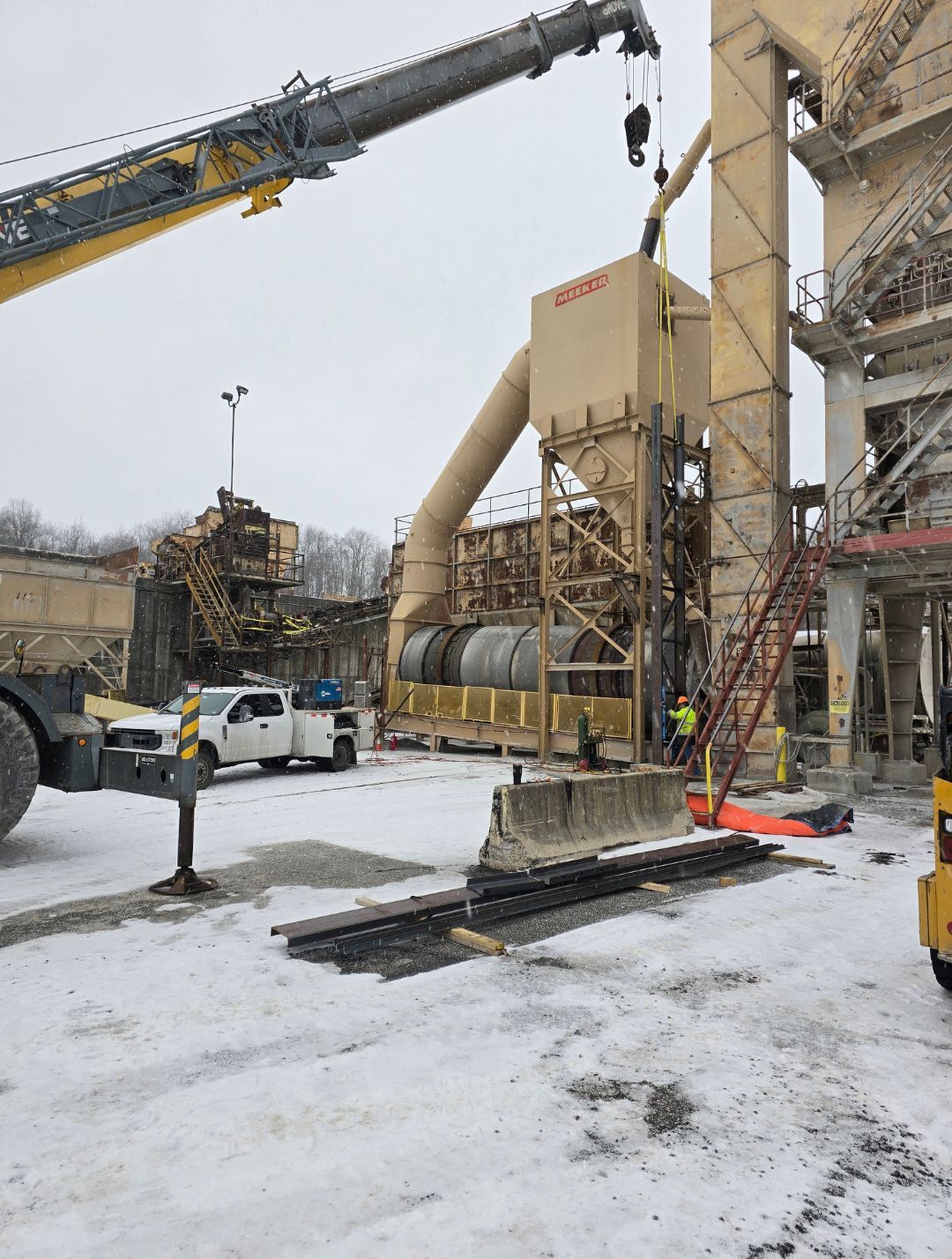 Crane and workers at a snowy industrial site beside a large silo and conveyor system