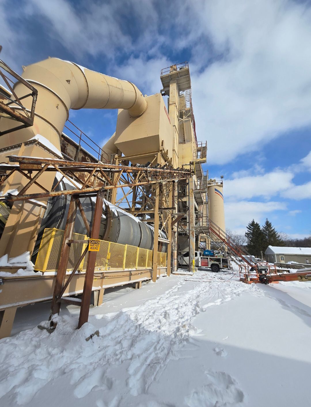 Snow-covered industrial facility with large beige ducts, metal framework, and blue sky