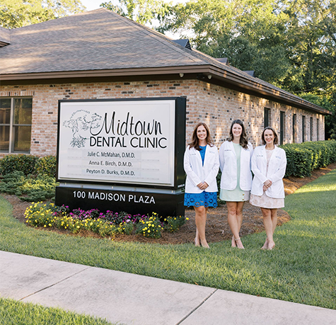 Three dentists in white coats stand in front of Midtown Dental Clinic sign.