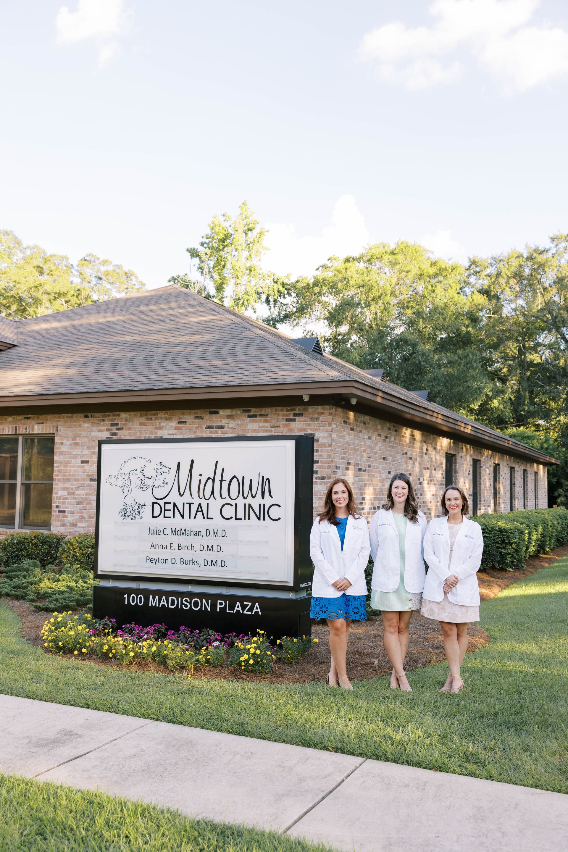 Three women in white coats stand in front of a dental clinic sign.