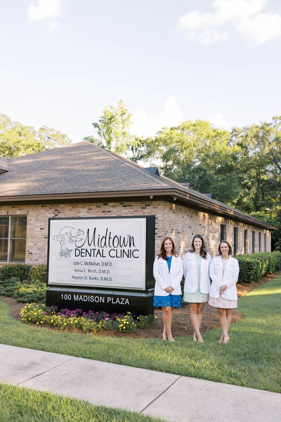 Three women in white coats stand in front of a dental clinic sign.