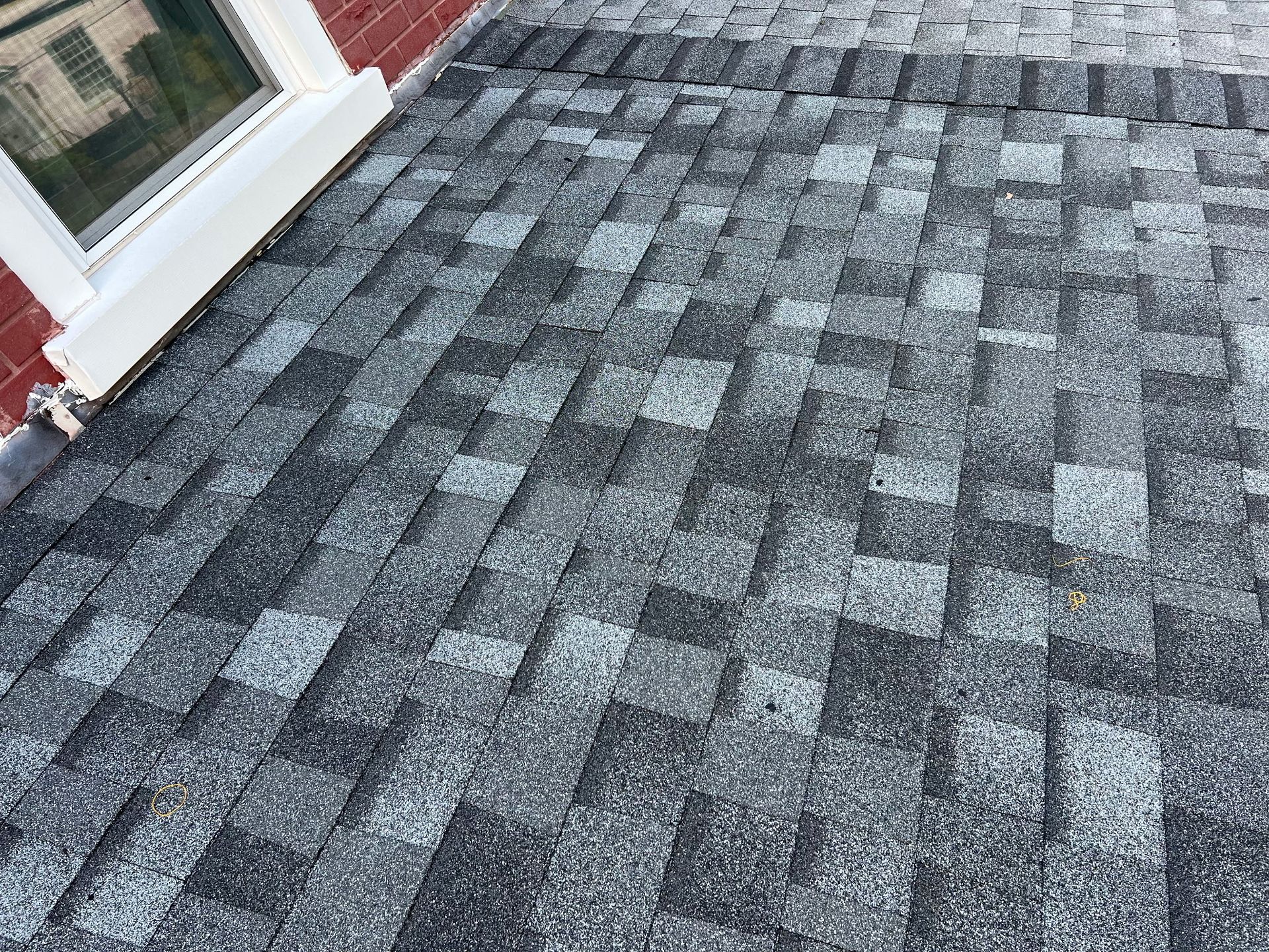Close-up view of a shingled roof with a variety of gray and black colors, next to a white window frame.