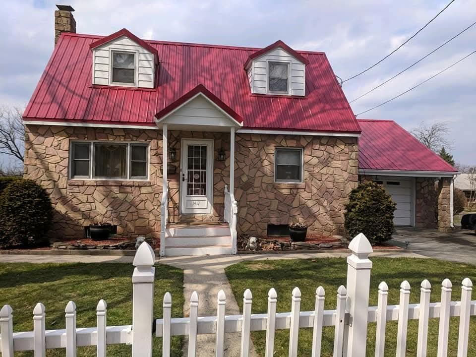 Stone house with red metal roof, white picket fence, and dormer windows.