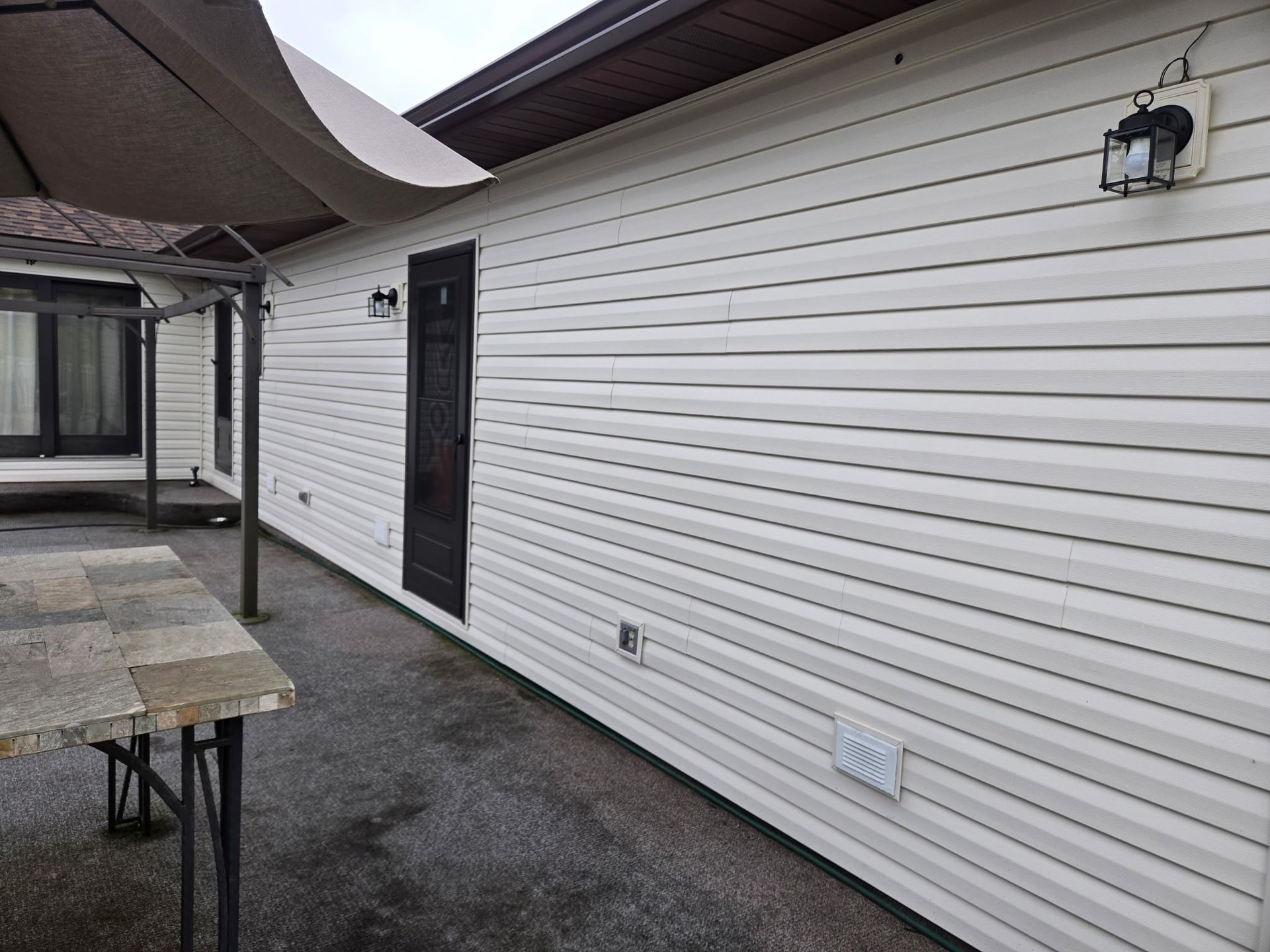 White vinyl siding on a house exterior, with a dark door and patio area.
