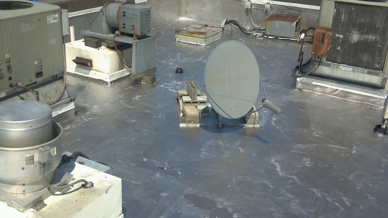 Rooftop with various mechanical units and a satellite dish on a reflective surface.