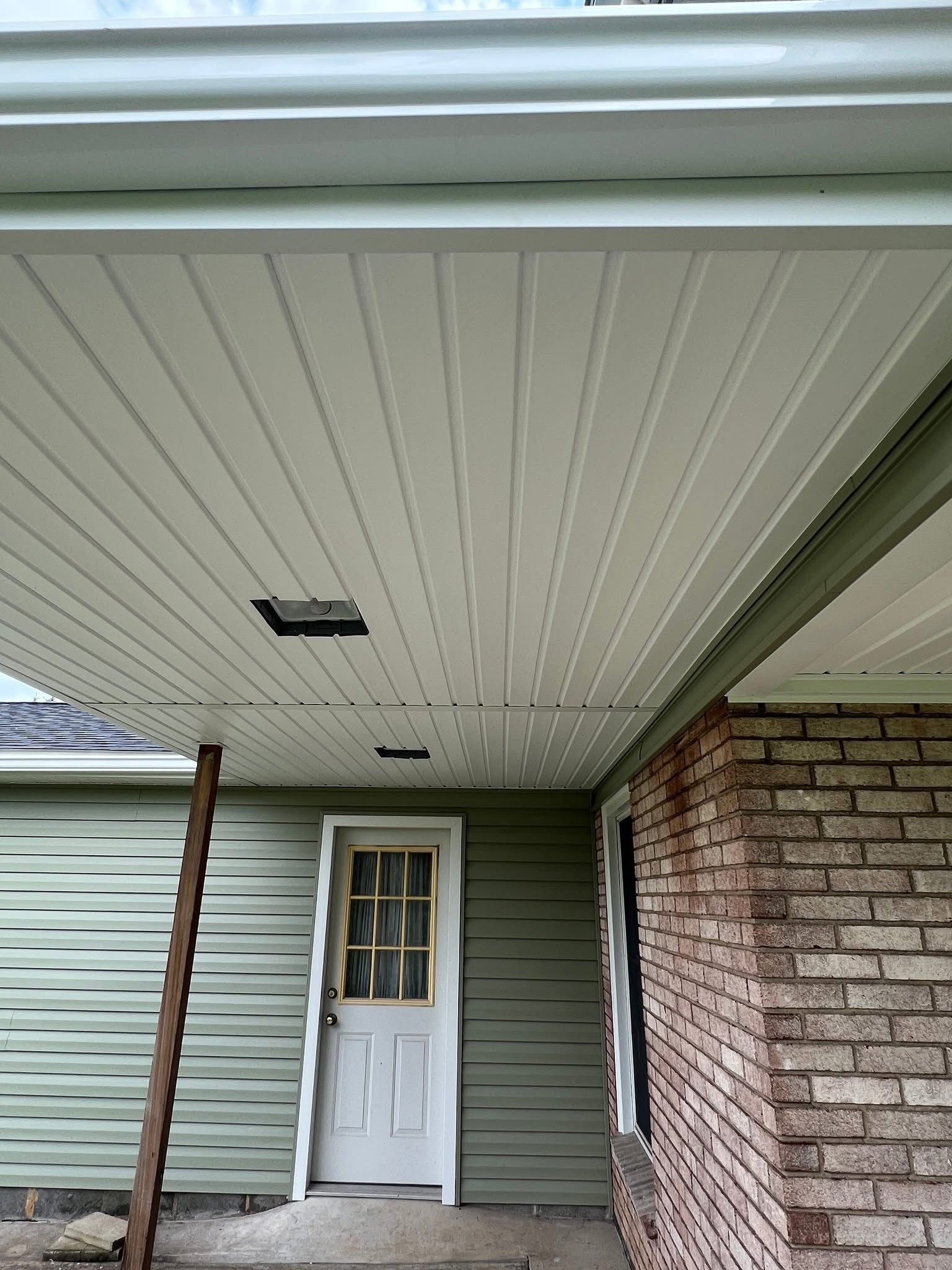 Green siding and white ceiling with recessed lighting above a white door and brick wall.