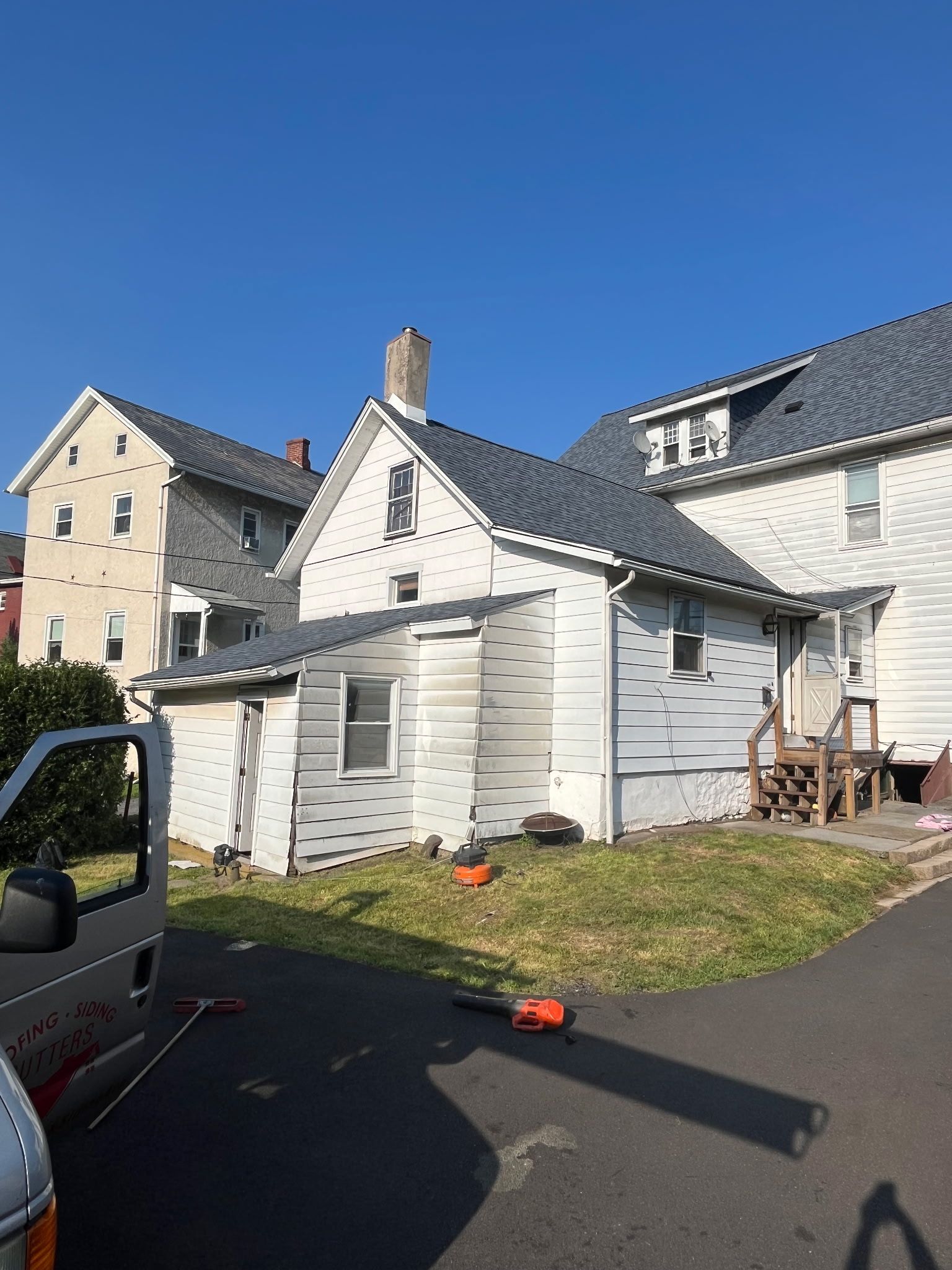 White house with gray roof, chimney, and surrounding green grass under a clear blue sky.