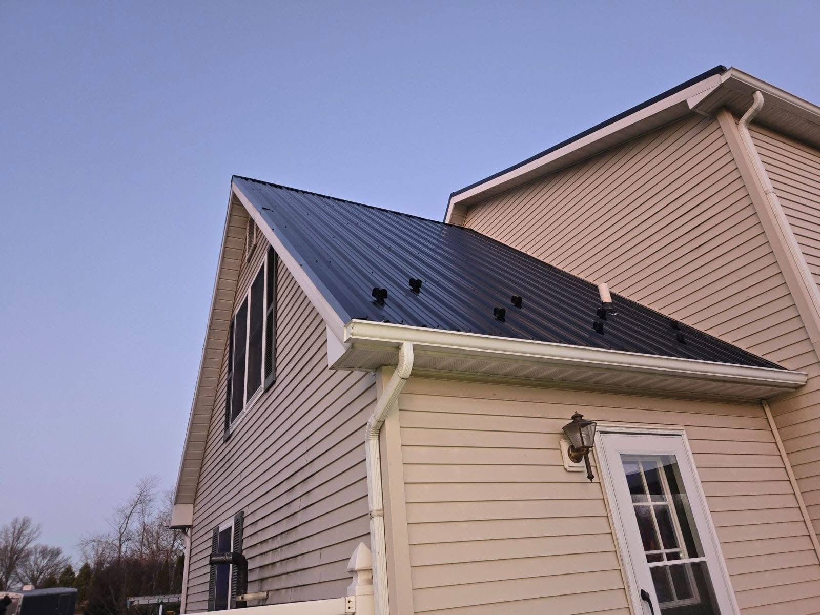 Black metal roof on a beige house against a clear blue sky.