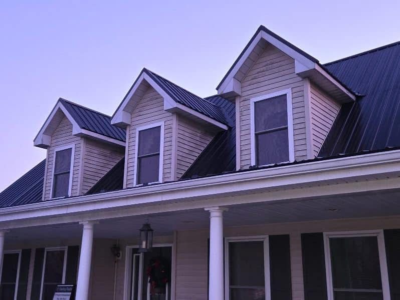 House exterior with dormers, porch, and black metal roof against a dusky sky.