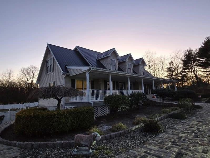 Two-story house with a large porch and dark roof at dusk; stone walkway leads to the entrance.