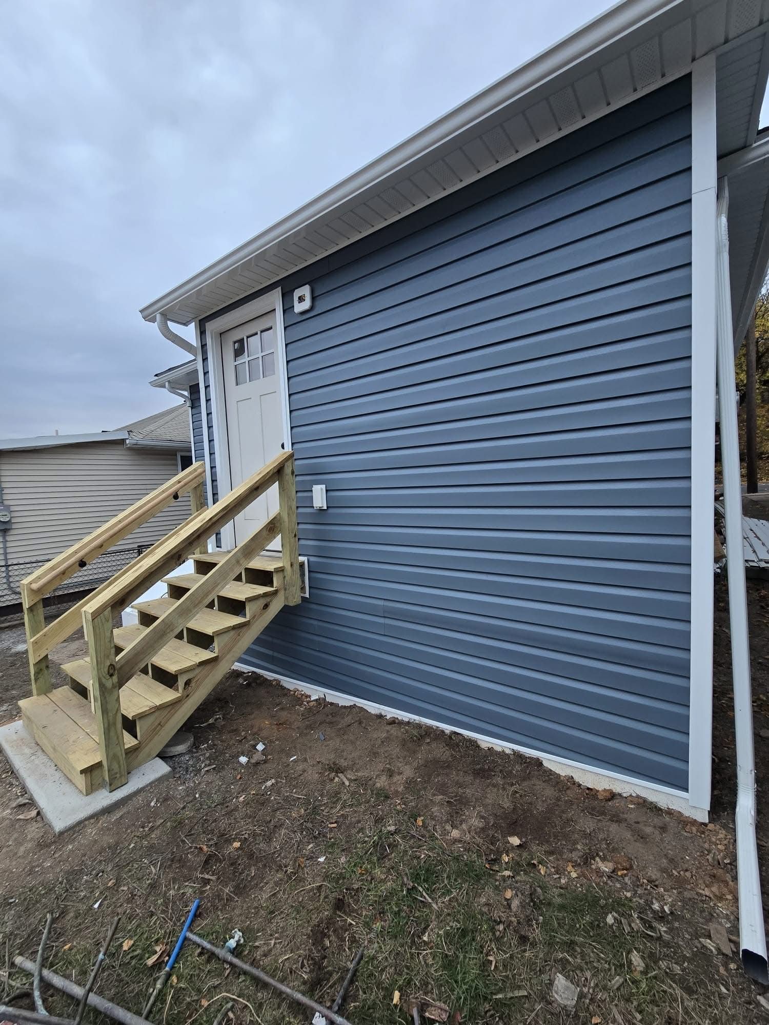 Exterior view of a building with a blue siding, white trim, and wooden stairs leading to a white door.