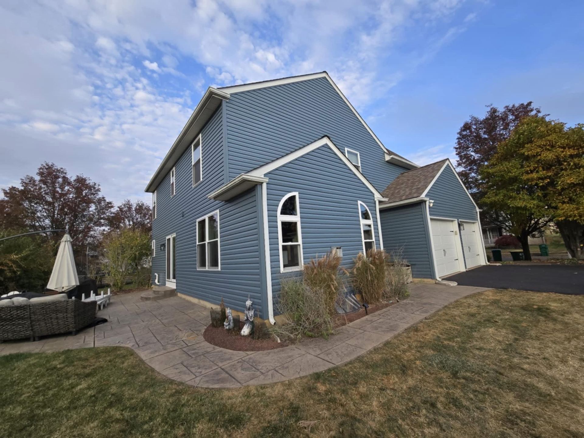 Blue-sided house with a stone patio, garage, and yard under a blue sky.