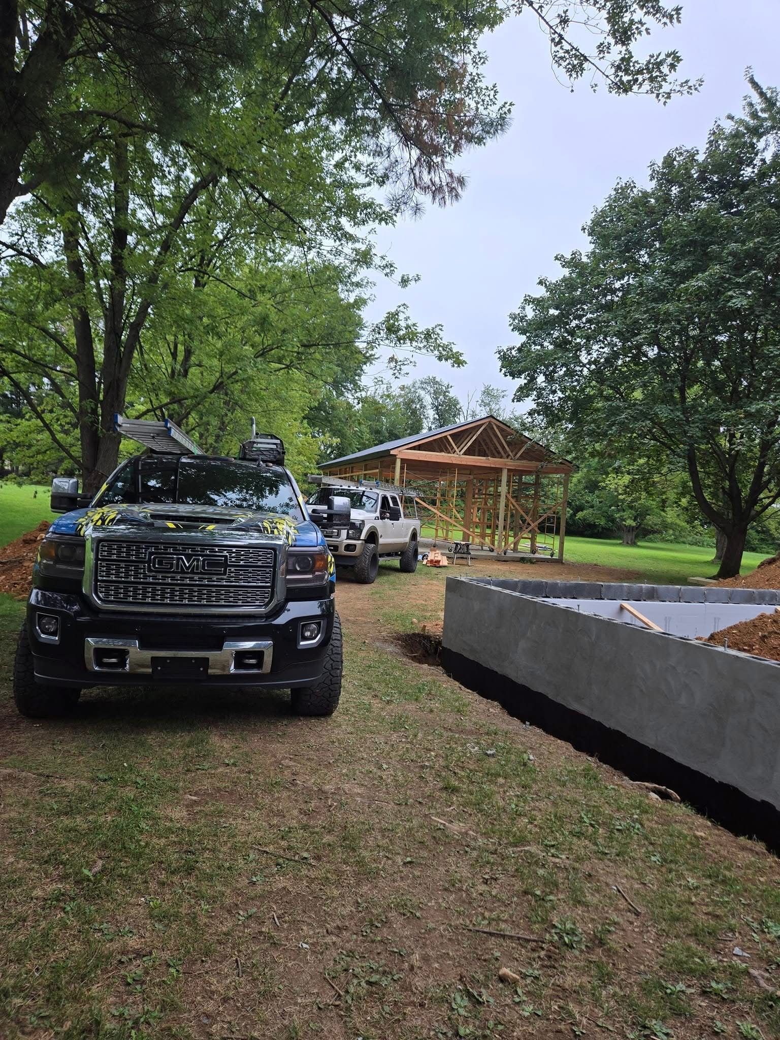 Black truck parked in a grassy yard, with a white truck behind it. A wooden structure is in the background.