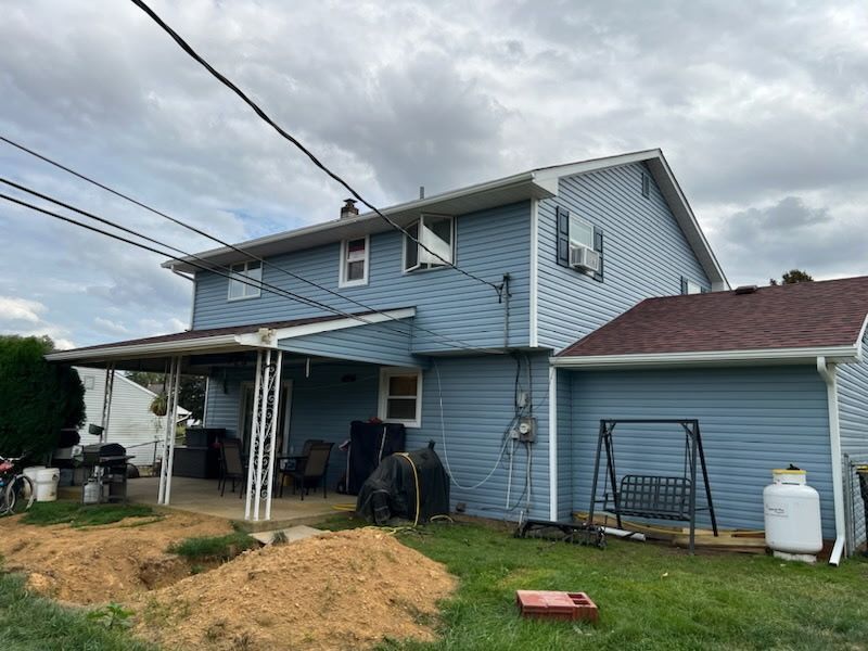 Two-story blue house with porch, outdoor swing, propane tank, and overcast sky.