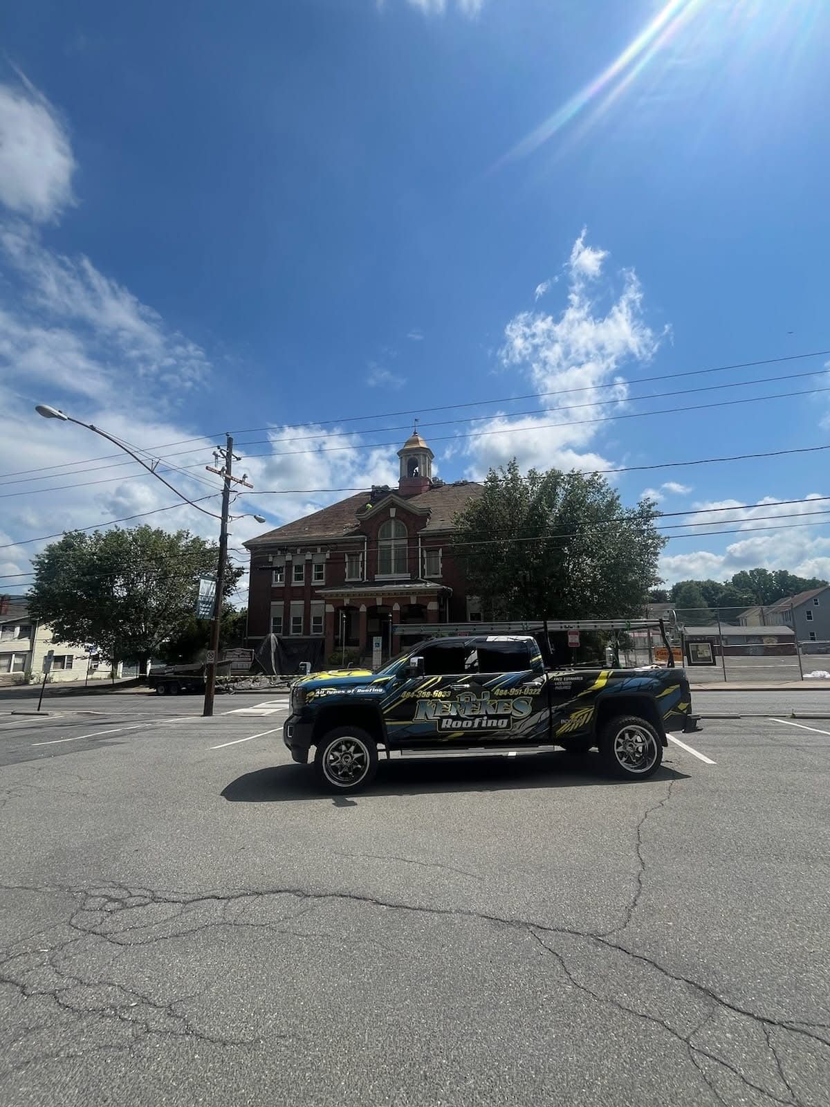 Truck parked in front of a brick building on a sunny day with blue sky and utility poles.