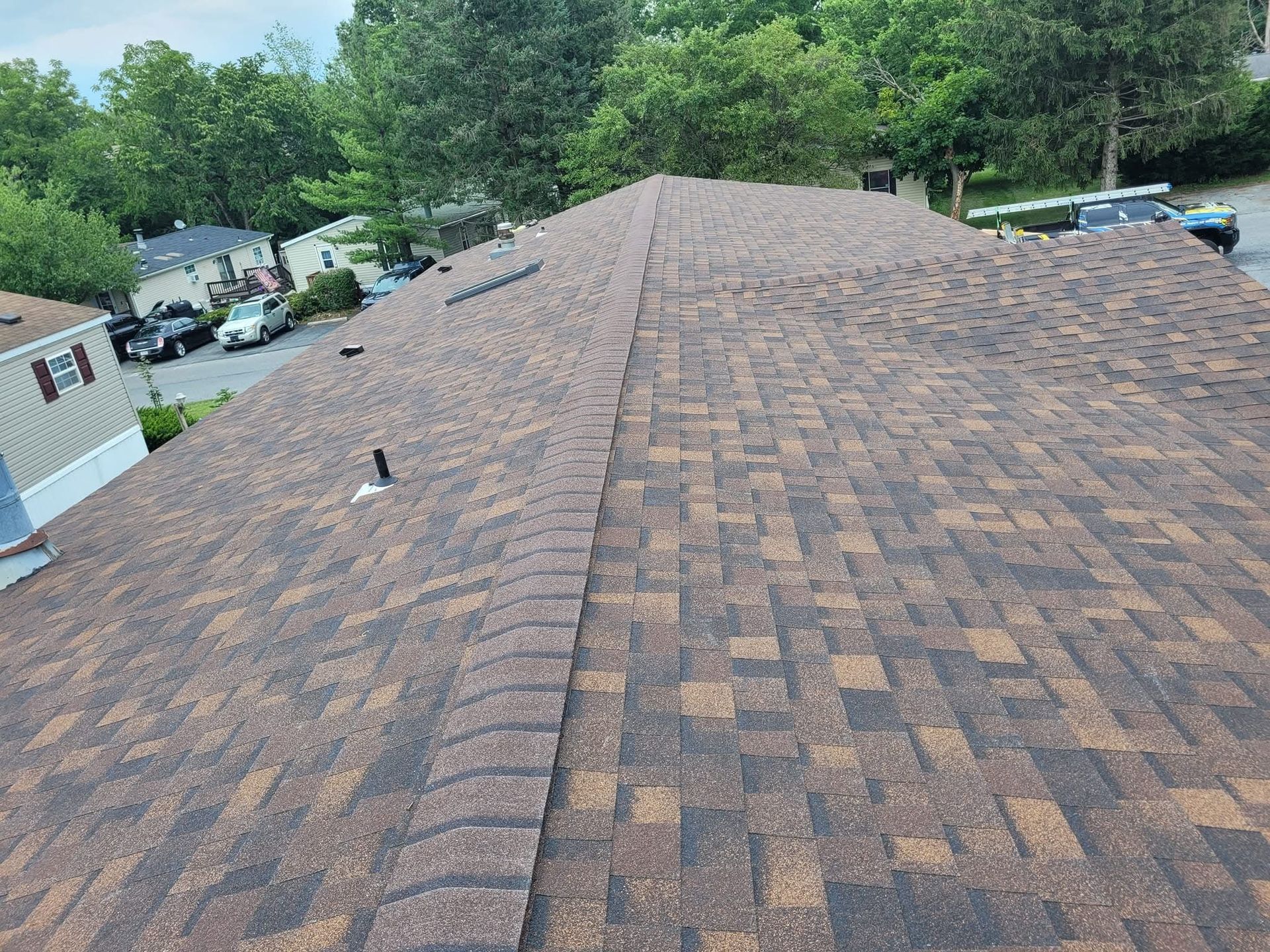 Brown asphalt shingle roof, angled view. Houses and trees in the background.
