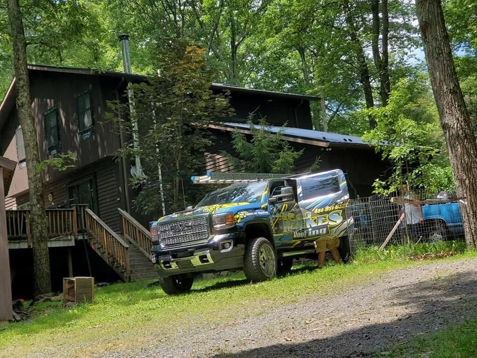A large truck with a colorful design parked in front of a two-story wooden house with a deck.