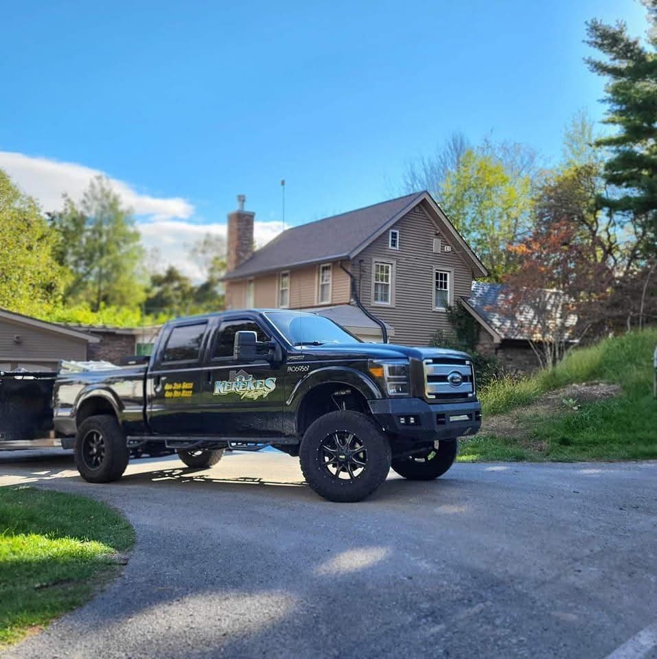 Black pickup truck parked in front of a stone house on a sunny day.