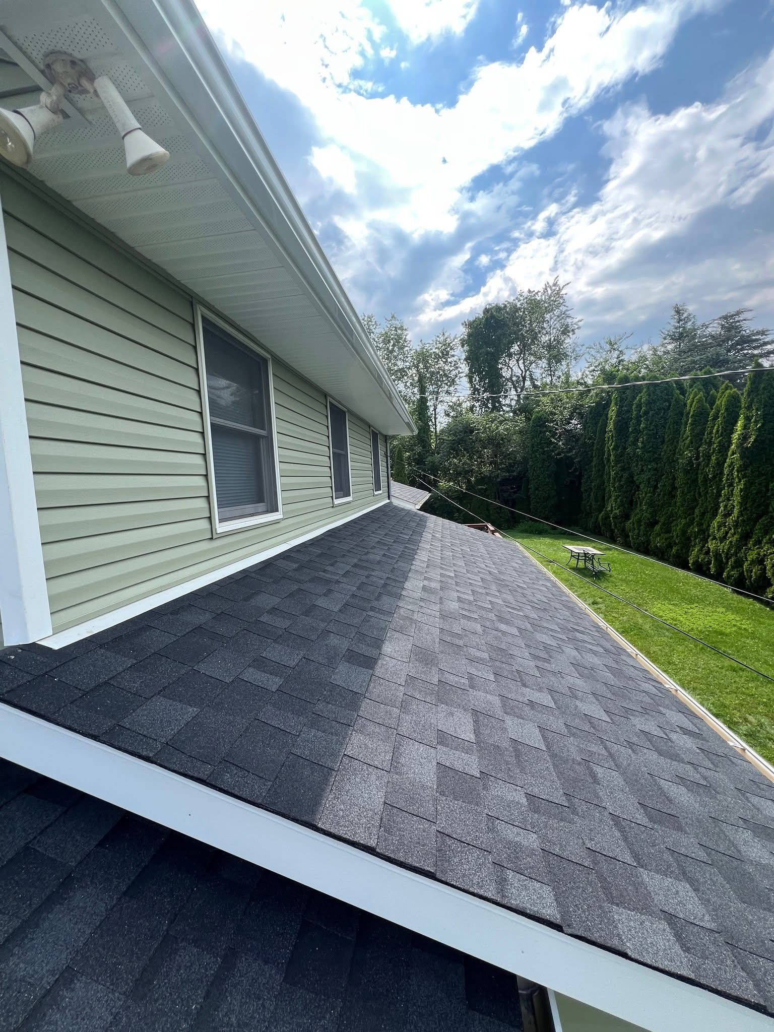 Green house with dark gray shingles, white trim, and a blue sky.
