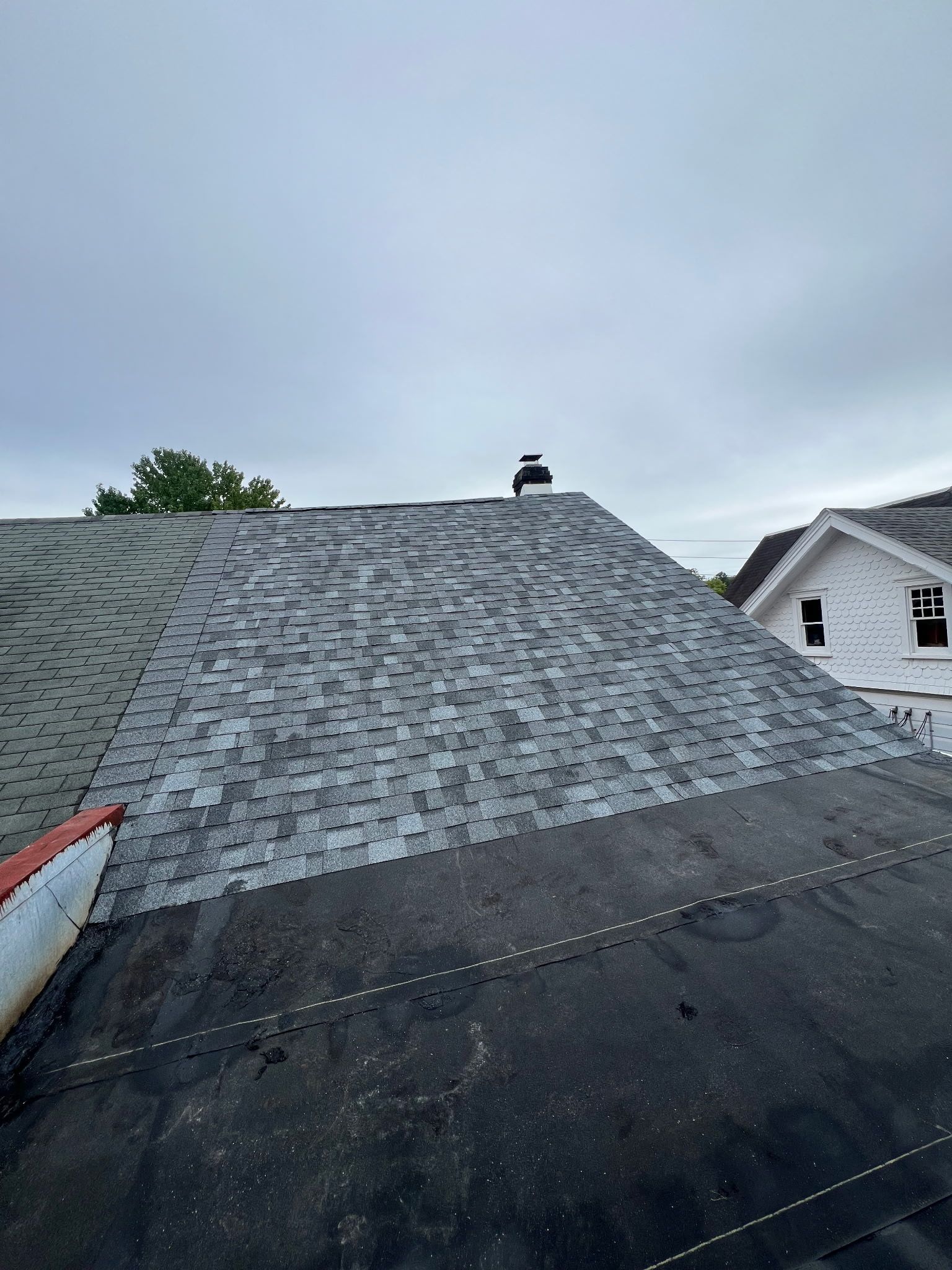 Dark roof with gray shingles and black tar. Chimney visible against a cloudy sky.