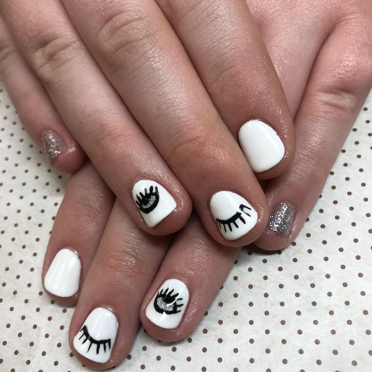 A woman 's nails are painted white with black eyes on them