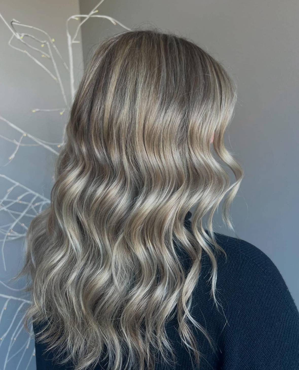 A woman with long wavy blonde hair is wearing a black sweater.