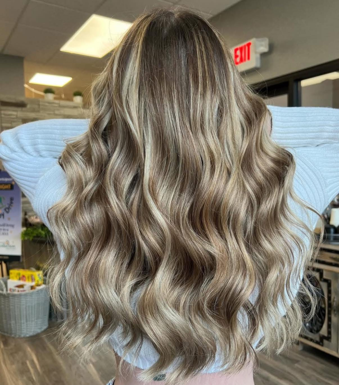 A woman with long wavy blonde hair is wearing a blue sweater.