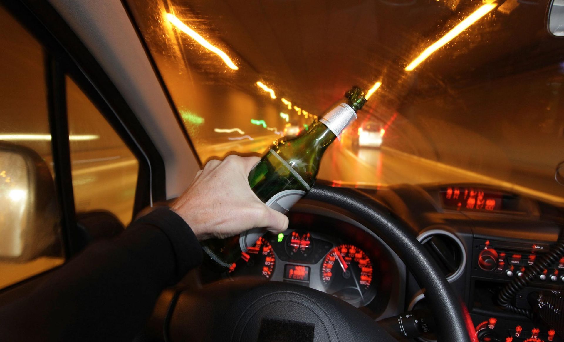 A person is driving a car with a bottle of beer in their hand.