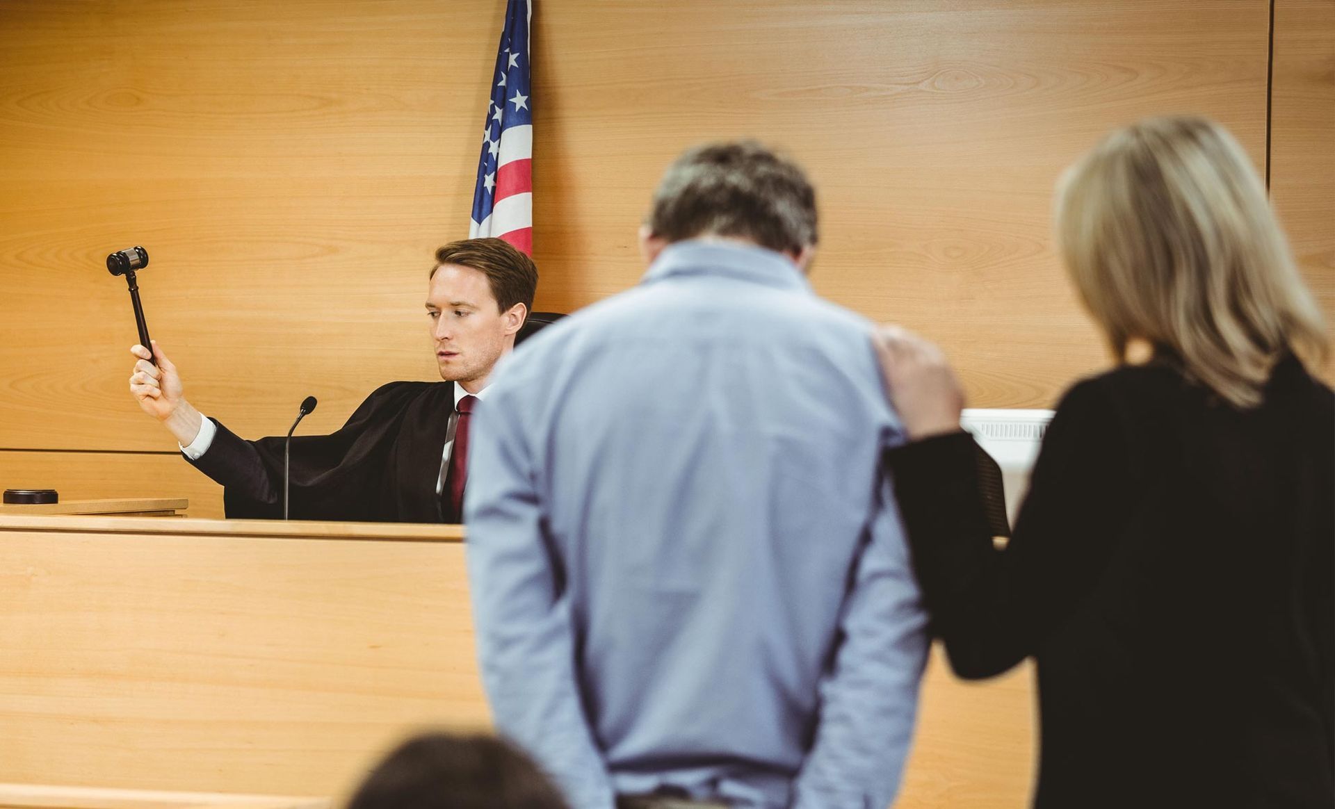 A man is standing in front of a judge in a courtroom holding a gavel.