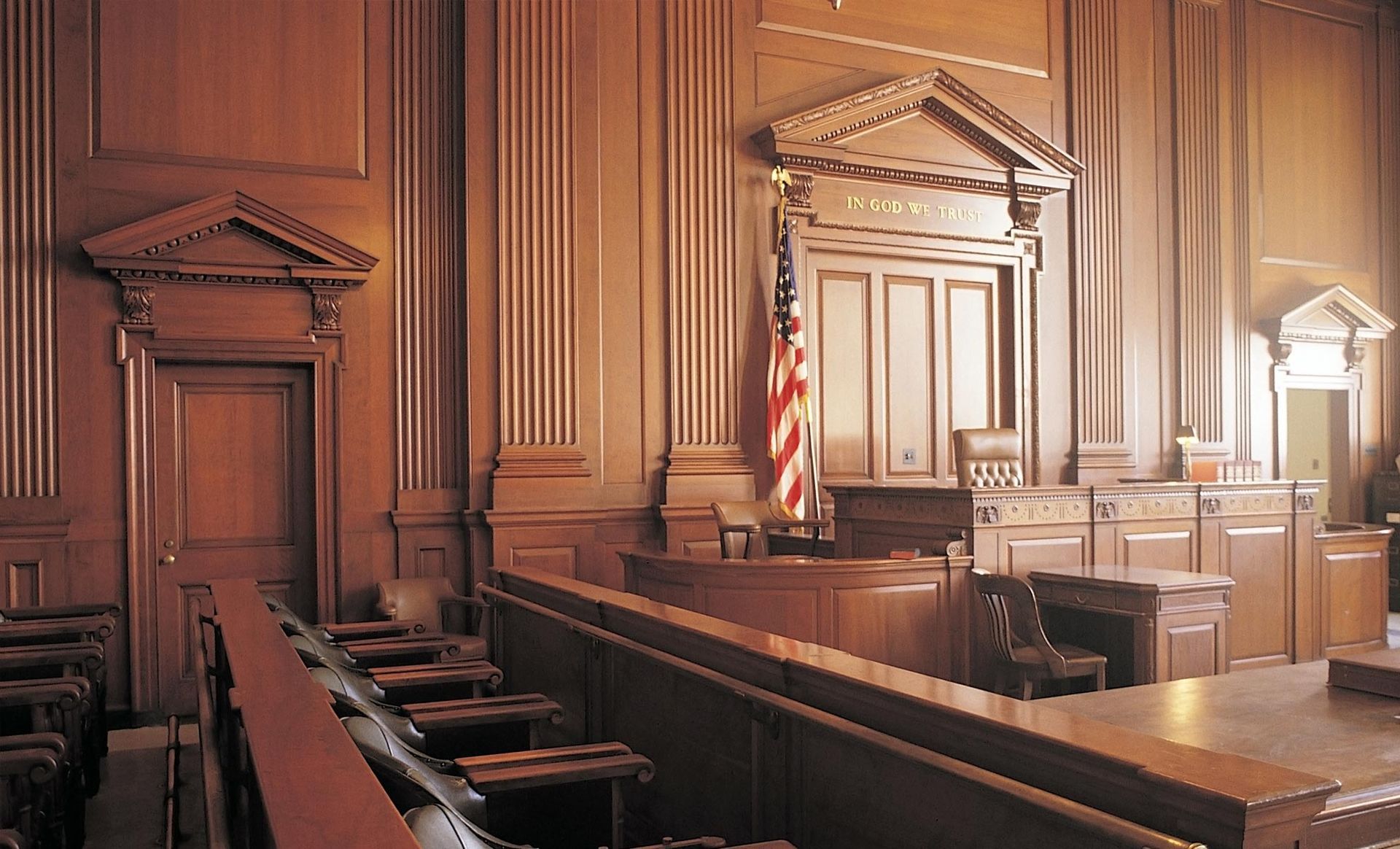 An empty courtroom with wood paneling and an american flag