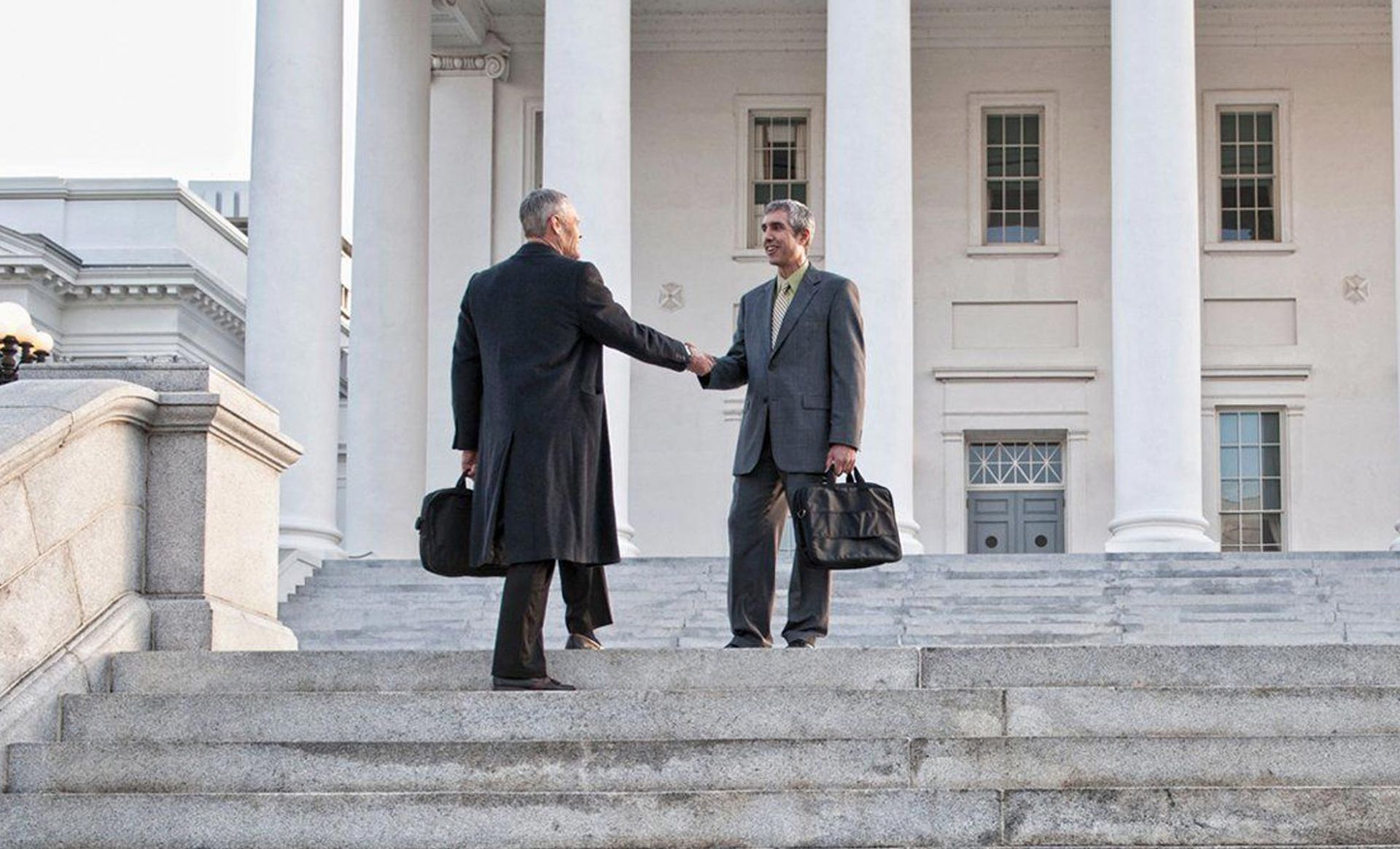 Two men are shaking hands on the steps of a building.