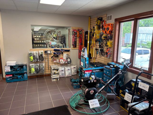 Inside a store, shelves of colorful hardware and tools line a tiled room near a window.